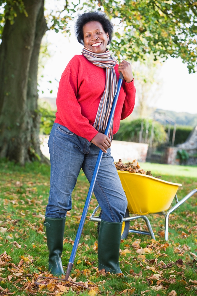 Mature woman collecting autumn leaves in garden
